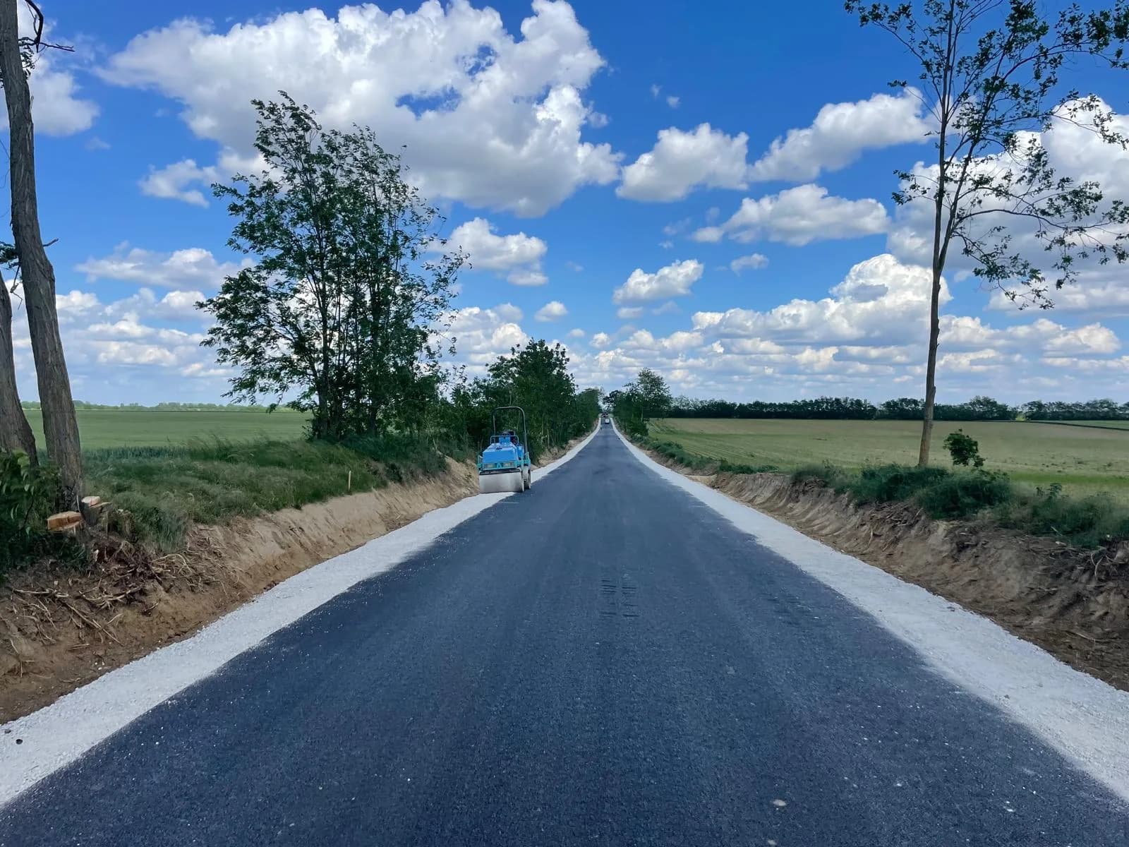 Frissen aszfaltozott, szegélyezett út mezőgazdasági területen